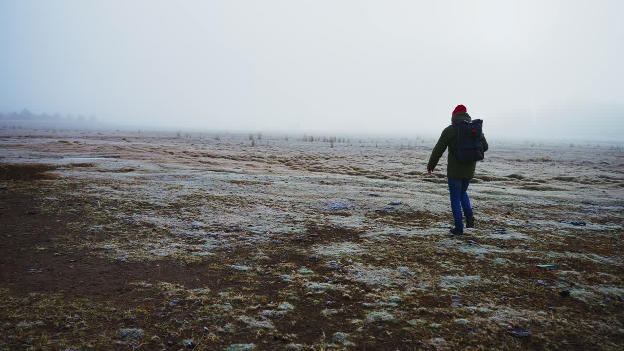 Persona che cammina in un campo nebbioso con uno zaino