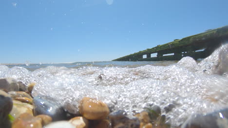 Eine-Niedrige-Aufnahme-Eines-Kiesstrandes-Mit-Der-Welle,-Die-Die-Kamera-Heraufkommt