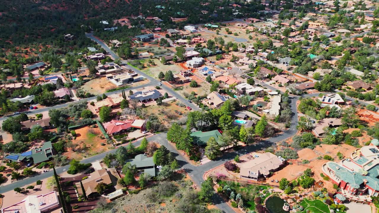 An aerial view showcases the Chapel of the Holy Cross nestled within Sedonas red rock formations, revealing residential areas and distant mountains under a bright, sunny sky
