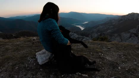niña sentada y abrazando a un perro labrador negro en una montaña