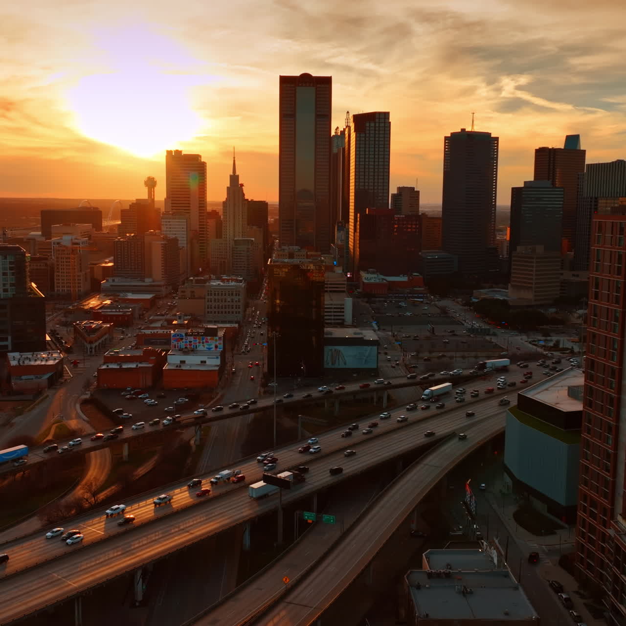 Pôr do sol sobre a paisagem urbana de Dallas, Texas, EUA. Numerosos veículos circulam pelas autoestradas ao anoitecer. Vista aérea.