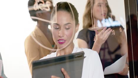 diverse businesswomen writing on glass wall and using tablet brainstorming at office, in slow motion