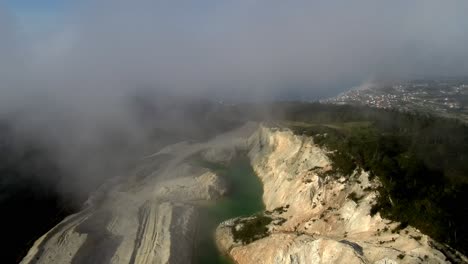 Vista-Aérea-A-Través-De-Nubes-Rodantes-De-Lago-Tóxico-Verde-En-La-Mina-Abandonada-De-Monte-Neme