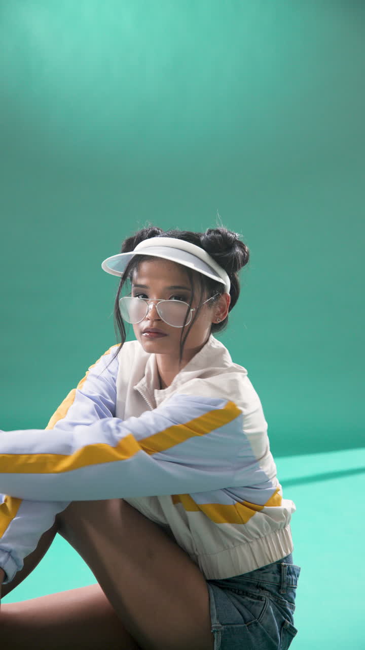 Vertical video: Young woman in stylish visor and jacket posing confidently in studio