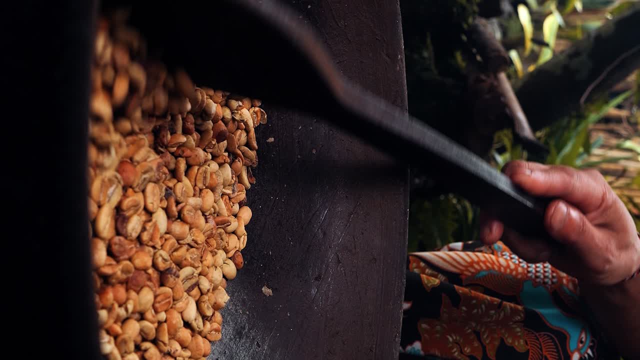 Vertical Medium shot of beans of the expensive kopi luwak coffee being stirred and roasted in a wok with a wooden spoon by an employee of a coffee plantation in ubud, bali in indonesia