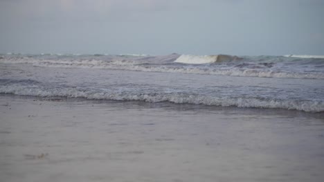 super slow motion shot of small waves rolling and breaking on beach shore during grey evening twilight after sunset