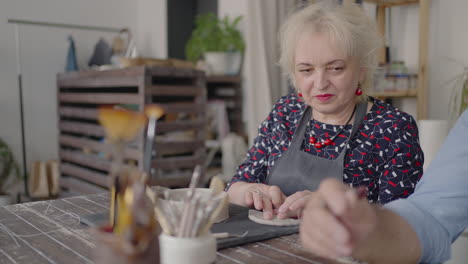 a group of elderly people at a master class in pottery together sculpt and cut a drawing on cups of clay for the manufacture of ceramic dishes