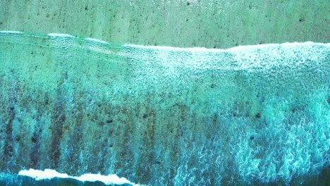 Big-ocean-waves-splashing-on-sandy-shore-of-tropical-island,-foaming-over-beautiful-sea-bottom-pattern-with-pebbles