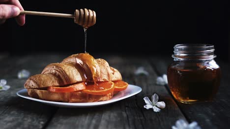 Imágenes-En-Cámara-Lenta-De-Miel-Goteando-Sobre-Un-Croissant-Lleno-De-Tres-Rodajas-De-Naranja