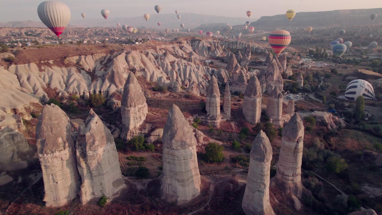 Un drone vola verso i camini delle fate e le mongolfiere della Cappadocia all'alba.