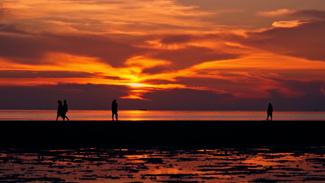 Silhouette di persone che camminano sulla spiaggia al tramonto