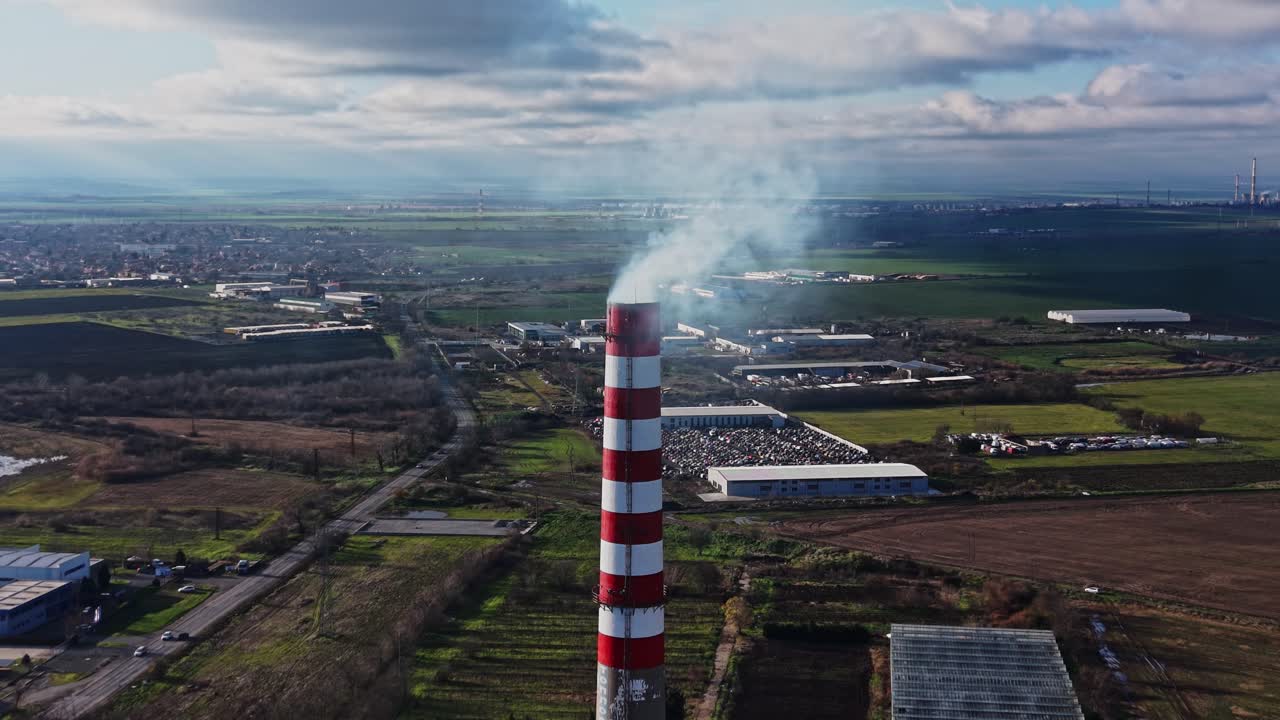 Grande ciminiera che rilascia fumo su un'area industriale di giorno