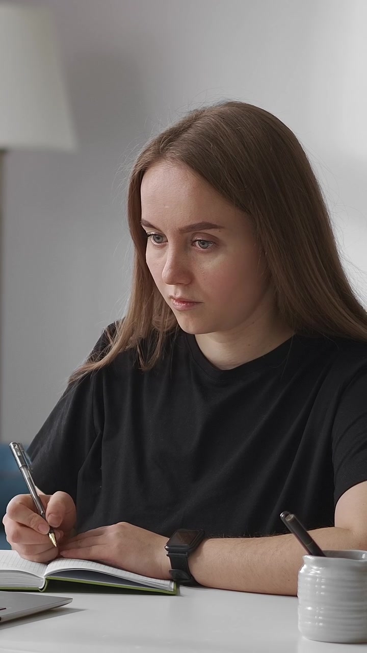 Giovane donna concentrata che scrive nel quaderno alla scrivania