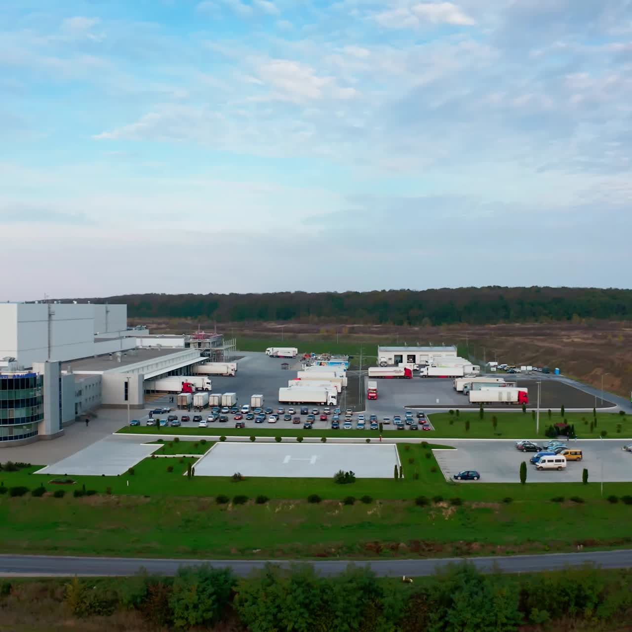 Modern industrial plant in nature. New industrial complex with car parking on field. Beautiful white building of a factory. Aerial view. Camera moves back.