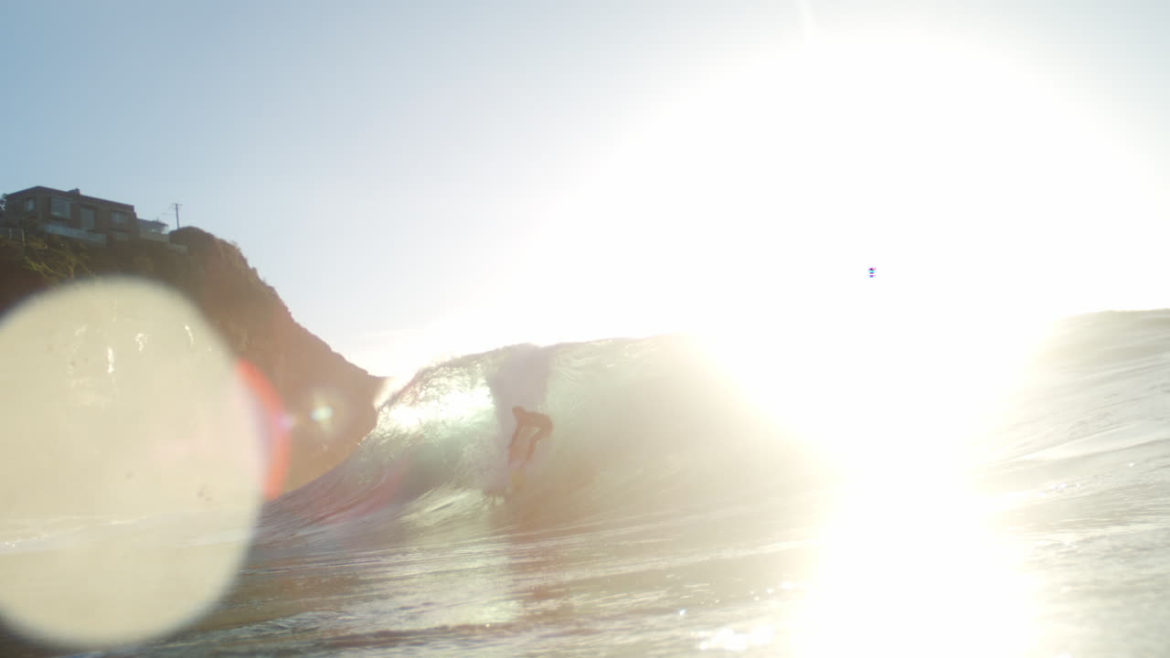 Sun flares through translucent wave in dramatic slow motion
