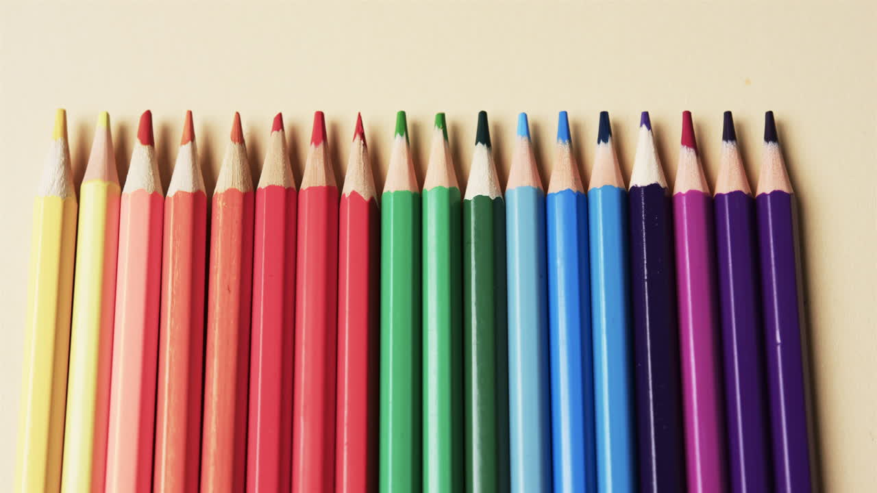 primer plano de lápices de colores dispuestos sobre un fondo beige, en cámara lenta