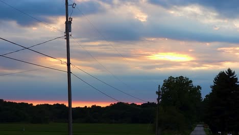 Shot-of-asphalt-road-along-picturesque-rural-countryside-illuminated-by-the-first-rays-of-sun-through-white-clouds