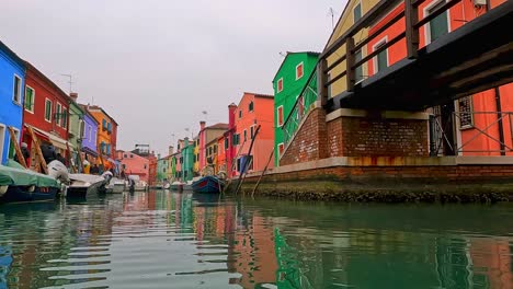 water surface pov view of burano picturesque colored houses and canal with moored boats, italy