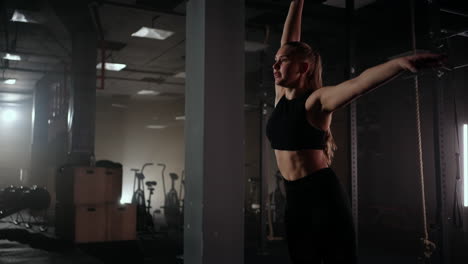 in slow motion a woman lifts a dumbbell over her head while working out in a dark gym. athletic strong woman performs a difficult workout with lifting dumbbells