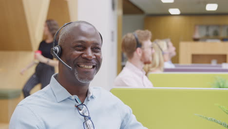 portrait of mature businessman wearing headset talking to caller in customer services centre