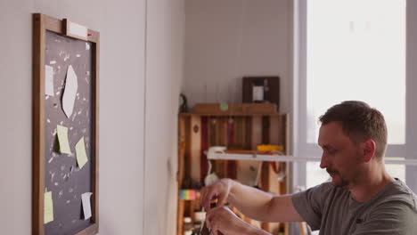 bearded leathersmith takes apron from chalkboard in workshop