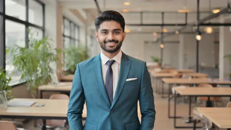 young confident entrepreneur wearing elegant suit is posing in coworking space with his hands in pockets, looking successful and happy about his job