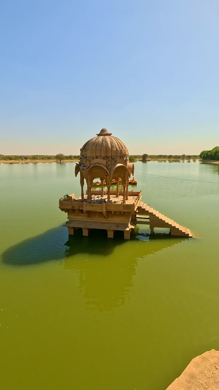 Gadsisar Lake in Jaisalmer sparkles under the golden Rajasthan sun, mirroring ancient elegant pavilions in calm water offering a serene escape in the heart of the desert's timeless beauty India
