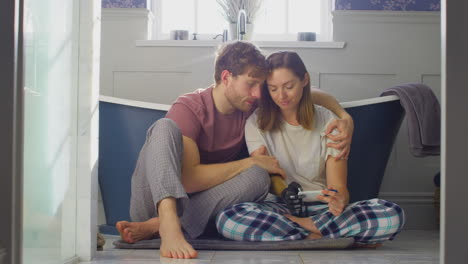 disappointed couple with woman with prosthetic arm sitting in bathroom with negative pregnancy test