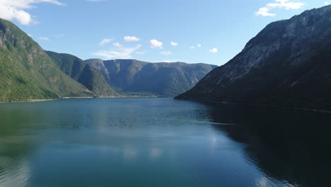 drone captures a calm fjord on norways west coast, bordered by lush green mountains and a clear blue sky.