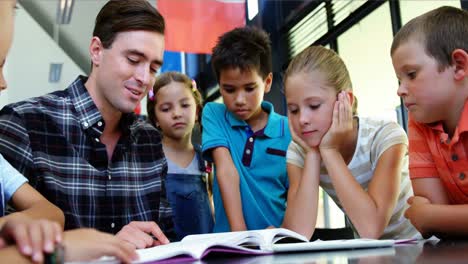 Niños-Escuchando-Al-Maestro-Mientras-Leen-Un-Libro-En-El-Aula