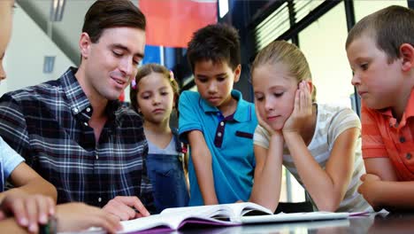 niños escuchando al maestro mientras leen un libro en el aula