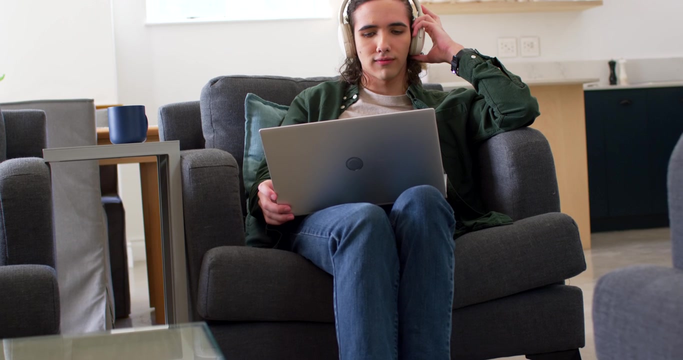 Camera lifting revealing African American man sitting at home on laptop adjusting headset for work