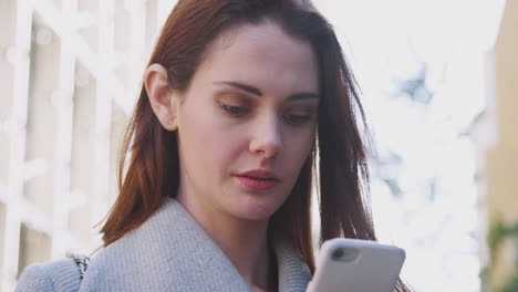 Close up of young white woman standing on a sunny street in London using her smartphone, close up, low angle