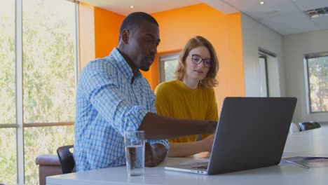 Junge-Geschäftskollegen-Gemischter-Abstammung-Diskutieren-Am-Laptop-In-Einem-Modernen-Büro-In-4K