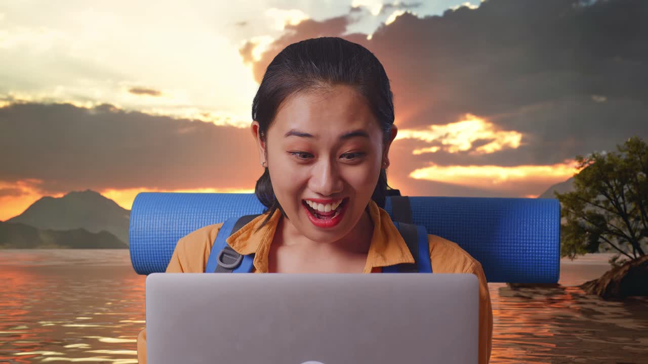 Close Up Of Asian Female Hiker With Mountaineering Backpack Looking At A Laptop And Saying Wow While Standing At A Lake During Sunset Time