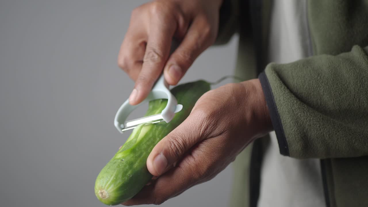 A person's hands peeling a fresh cucumber with a vegetable peeler