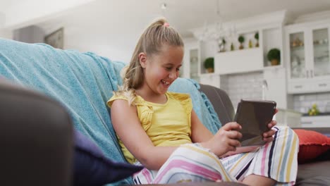 Glückliches-Kaukasisches-Mädchen-Zu-Hause,-Das-Mit-Einem-Tablet-Auf-Der-Couch-Sitzt-Und-Lächelt