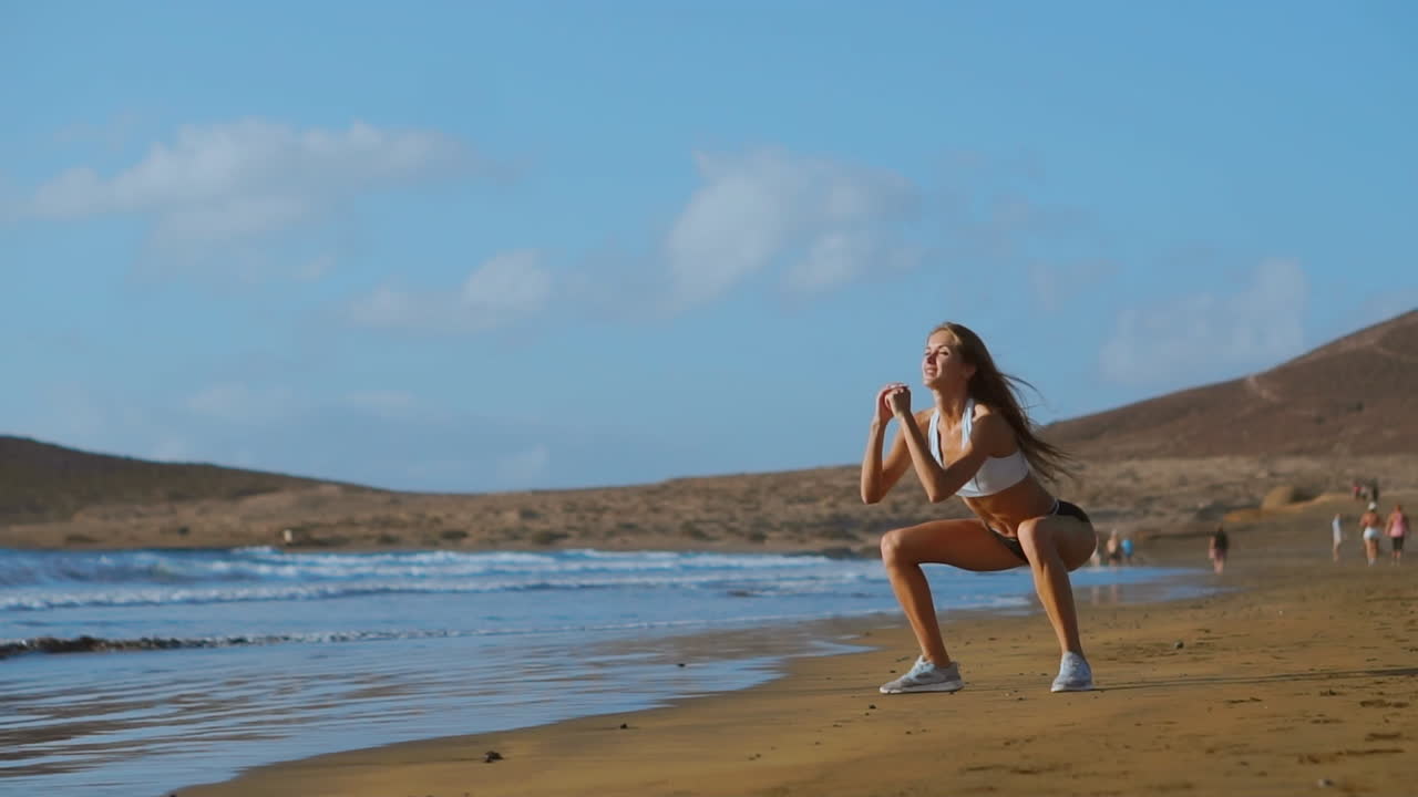 Atleta che indossa abbigliamento sportivo e fa squat all'aperto. Donna in forma che si allena in spiaggia al tramonto. Giovane donna atletica che pratica sport all'aria aperta.