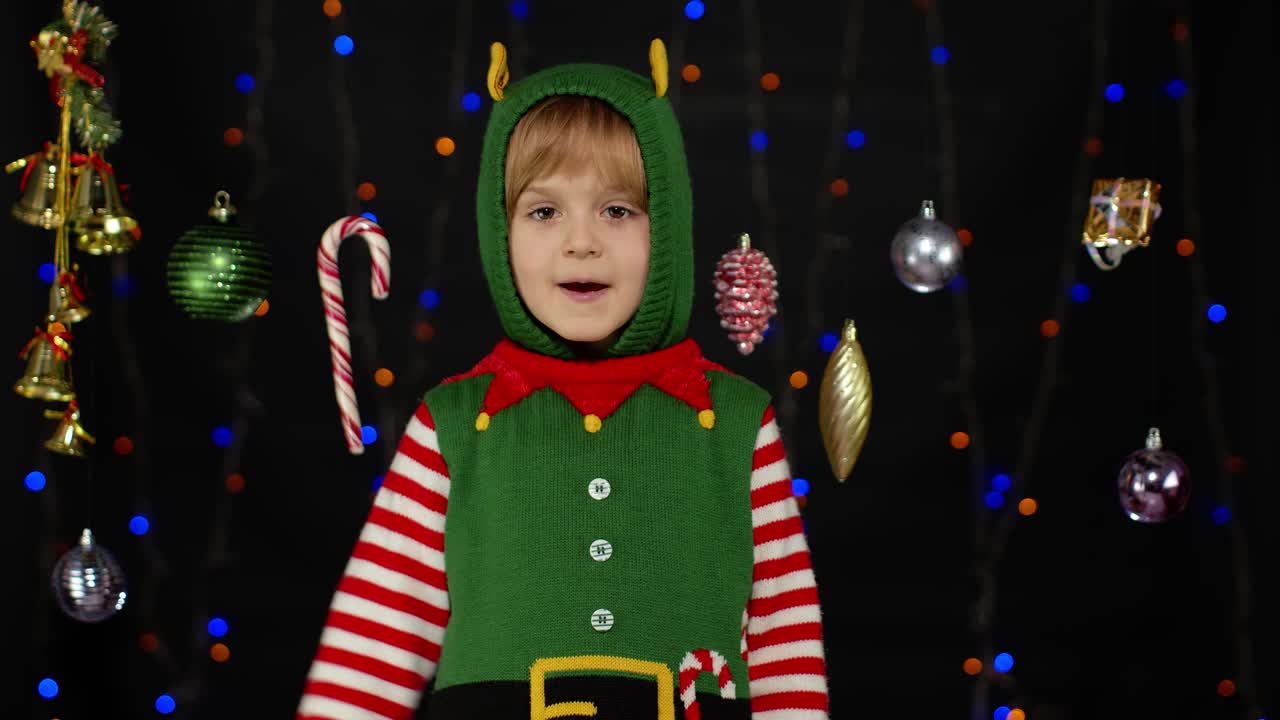 Dívka v kostýmu vánočního skřítka, pomocníka Santy, mává na pozdrav rukou. Ahoj, nazdar, gesto pozdravu.