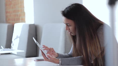 una hermosa chica sentada en la mesa en la oficina y usando su ipad