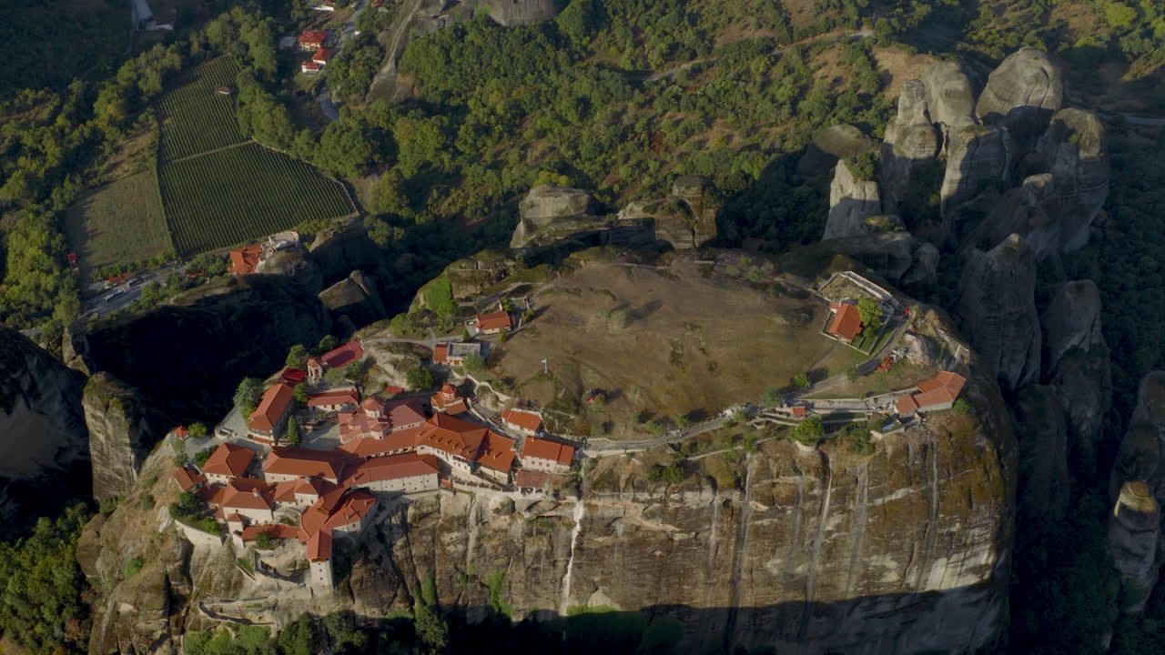 Cinematic aerial view of Meteora monastery in Greece perched on towering cliffs, dramatic rock formations and lush green valley create a breathtaking historic scene