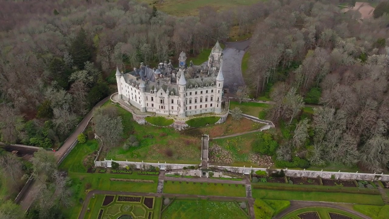 Riprese aeree con drone in volo verso il Castello di Dunrobin, Sutherland, Scozia, con torrette e guglie fiabesche che si ergono sopra giardini formali.