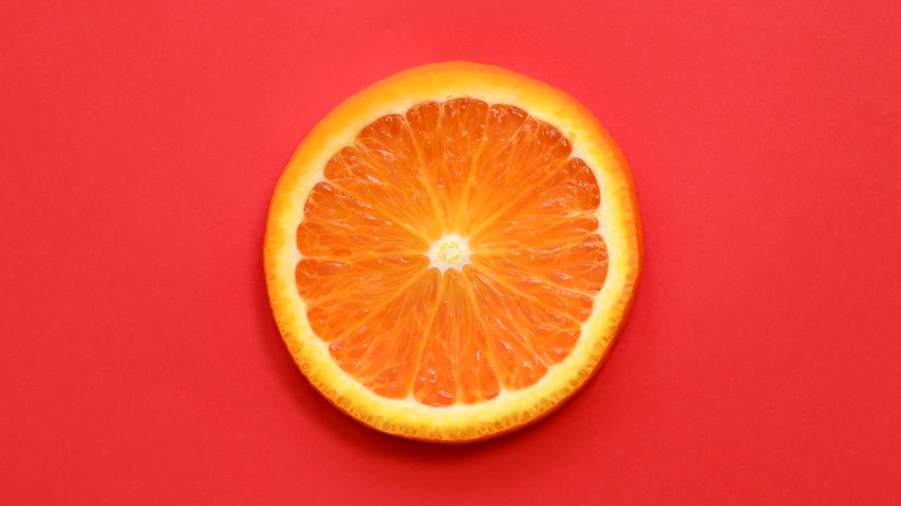 Slice of orange rotating top view on red background