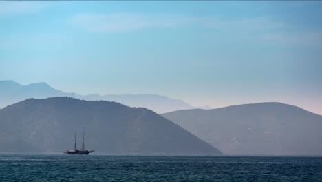 Un-Barco-Sereno-Navega-Por-Las-Aguas-De-Kusadasi-Con-Montañas-Brumosas-Al-Fondo.