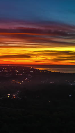 sunset to twilight hyperlapse over bali coastline with red and orange sky, aerial vertical shot