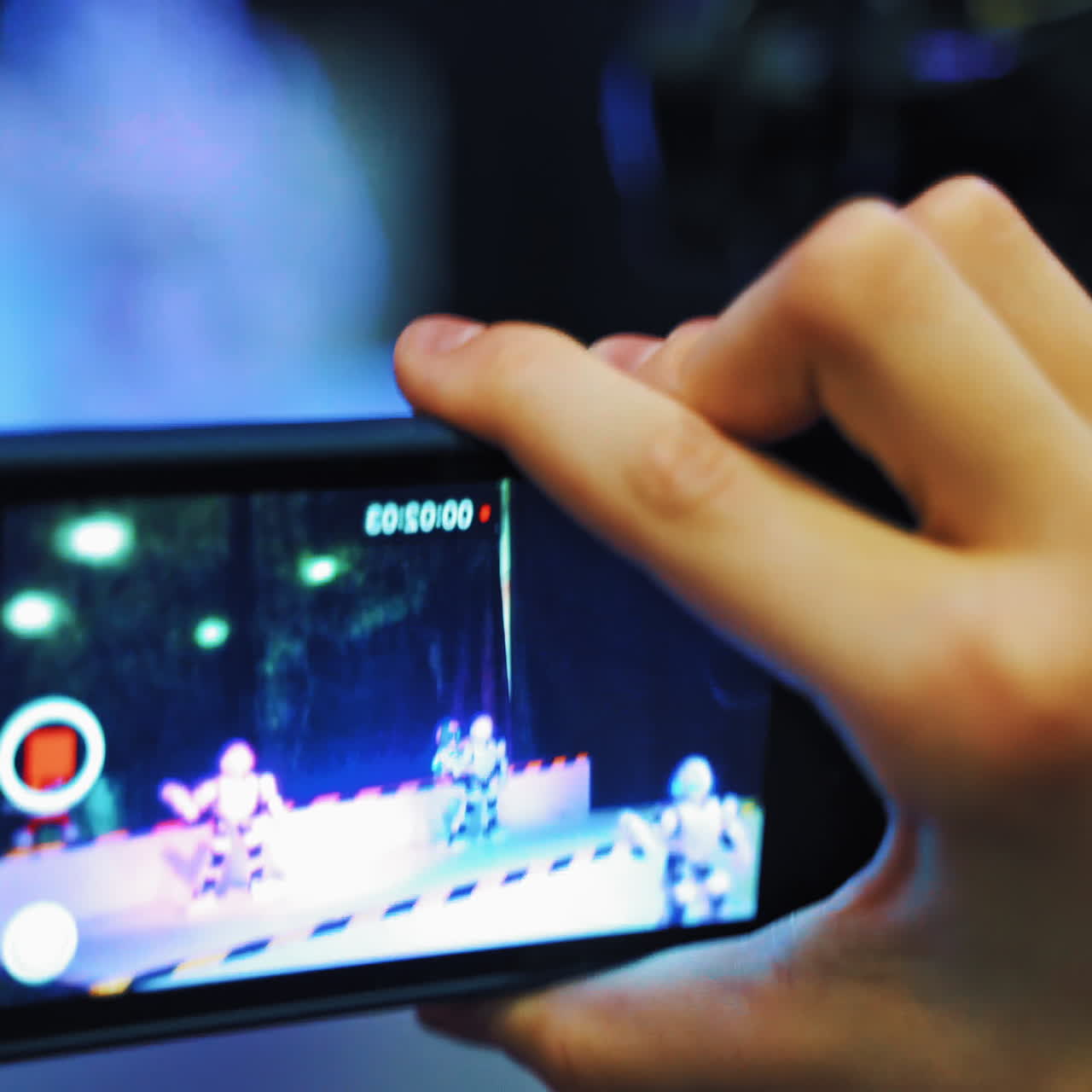 View of man's hand holding a mobile phone and taking pictures of dancing robots.