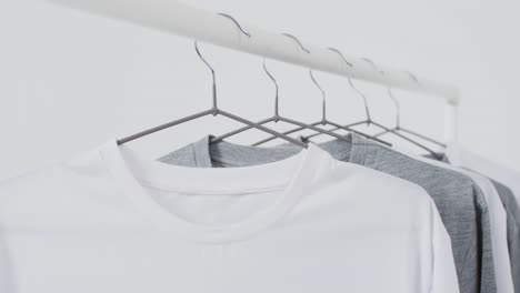 video of white and grey t shirts on hangers and copy space on white background