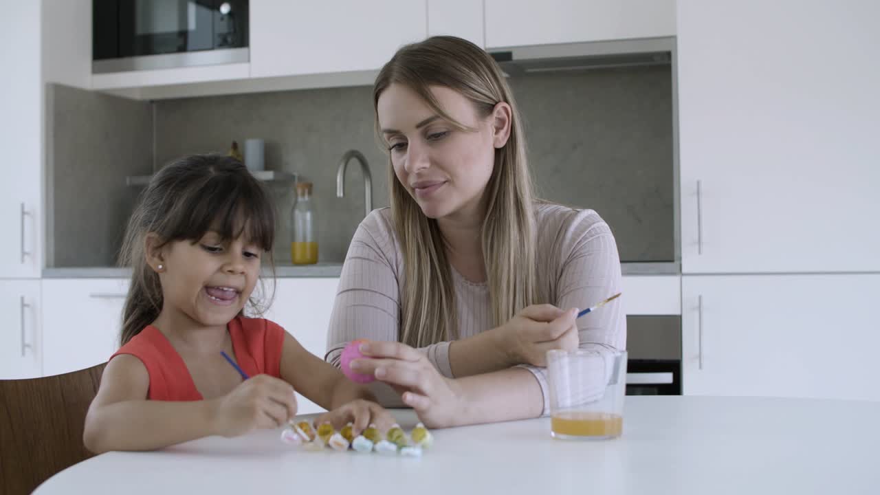 mamá ayudando a la niña a pintar el huevo en la mesa del comedor