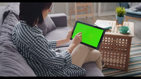 mujer usando una tableta en un sofá con una pantalla verde