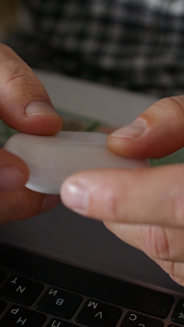Person holding wireless earbuds charging case on a laptop.